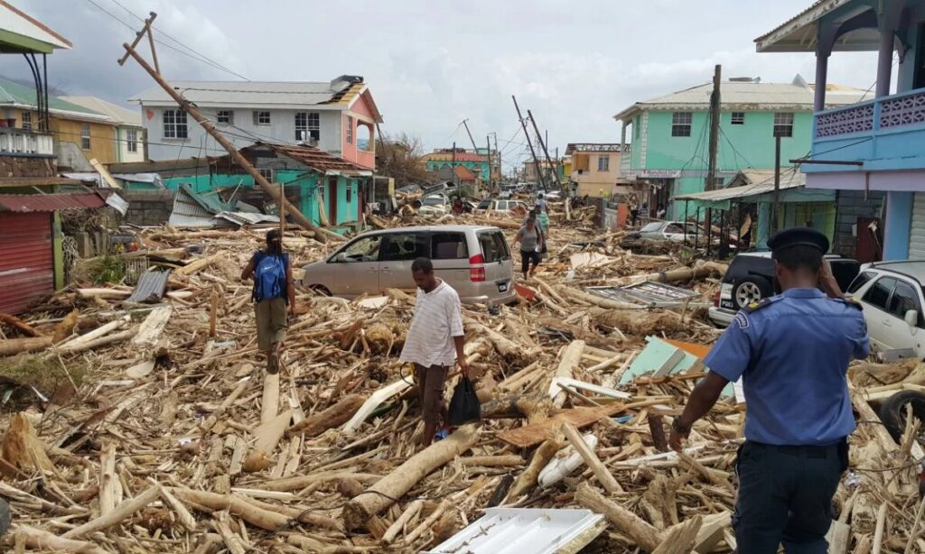 The aftermath of Hurricane Maria shows tons of debris and destruction as community members survey the damage on the island of Dominica. Photo by The Guardian 
