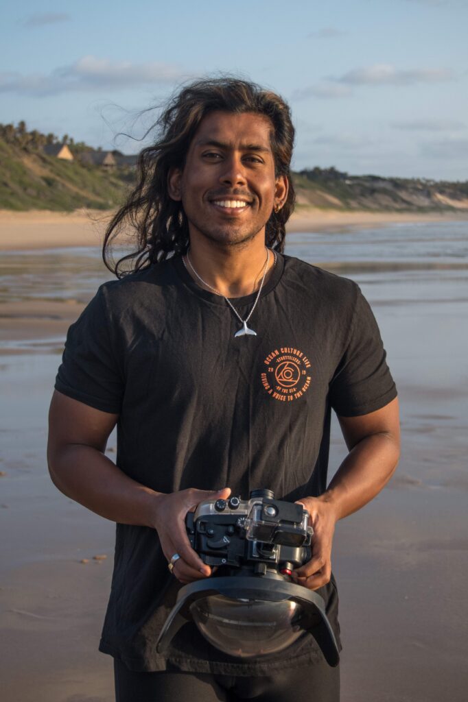 Headshot of Kaush Subramaniam standing on the beach with a camera