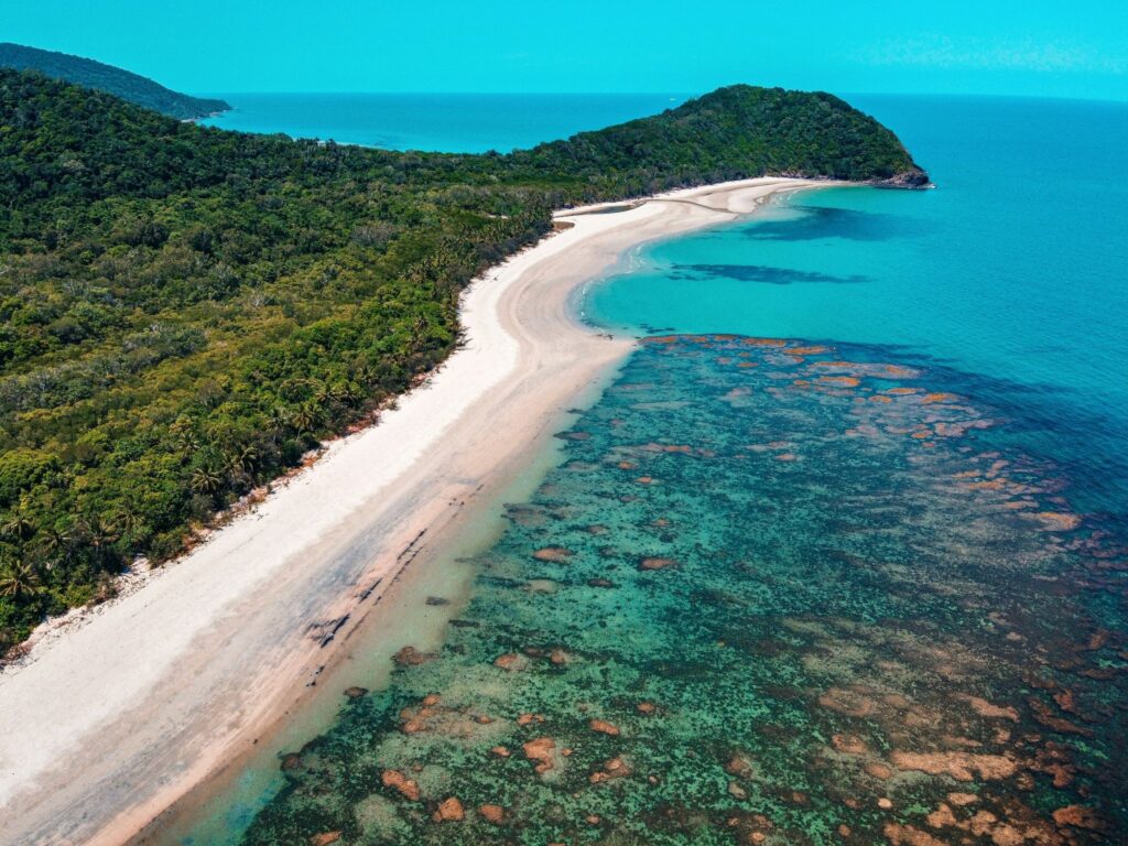 A spotted Great Barrier Reef on the coast of a deeply forested island and tall peninsula stretching out to sea