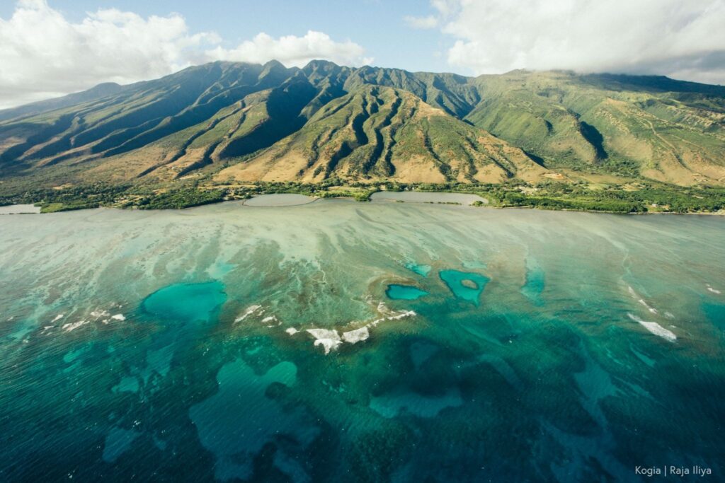 Aerial view of mauka to makai (mountain to see) with lush valleys and turquoise coral reef